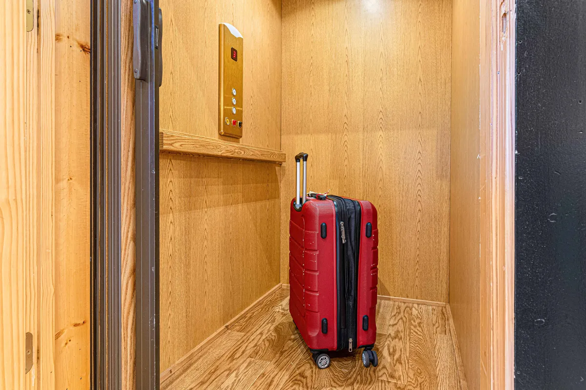 An interior shot of an elevator with elevator buttons, wood paneling, and a red suitcase, suggesting easy arrival and mobility throughout the home. The scene conveys the transitional experience of moving between floors without barriers.