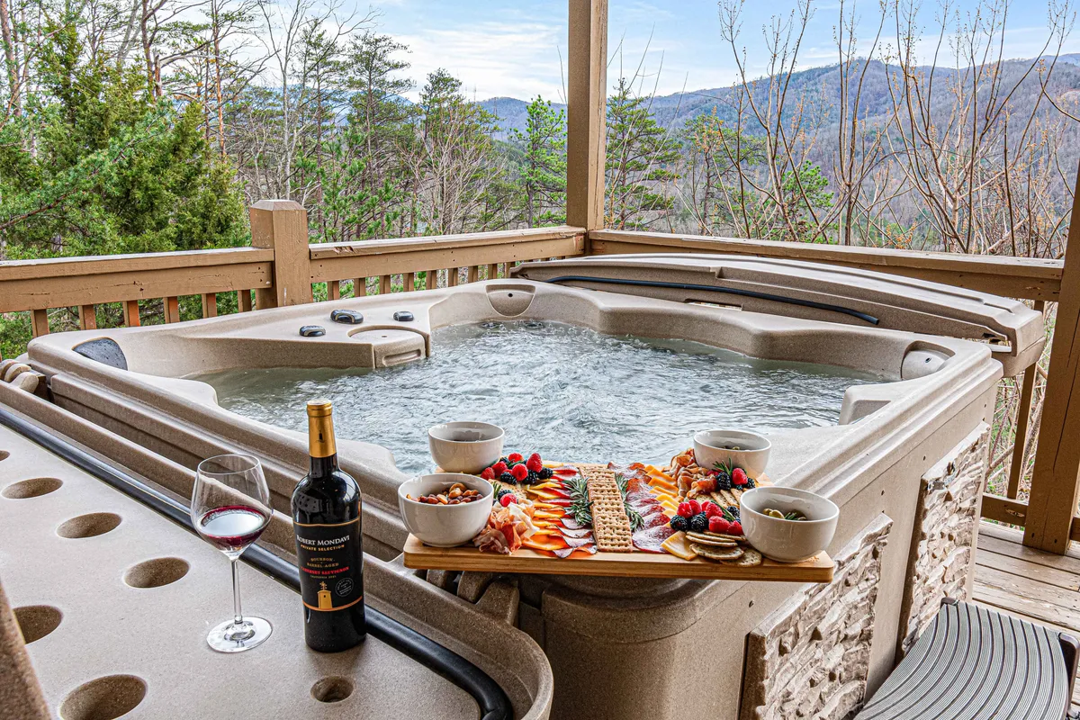 An inviting exterior hot tub on a deck, with a food platter, wine glass, and scenic mountain views. The setting is tranquil yet festive, highlighting the relaxation and celebratory atmosphere promised by the section.