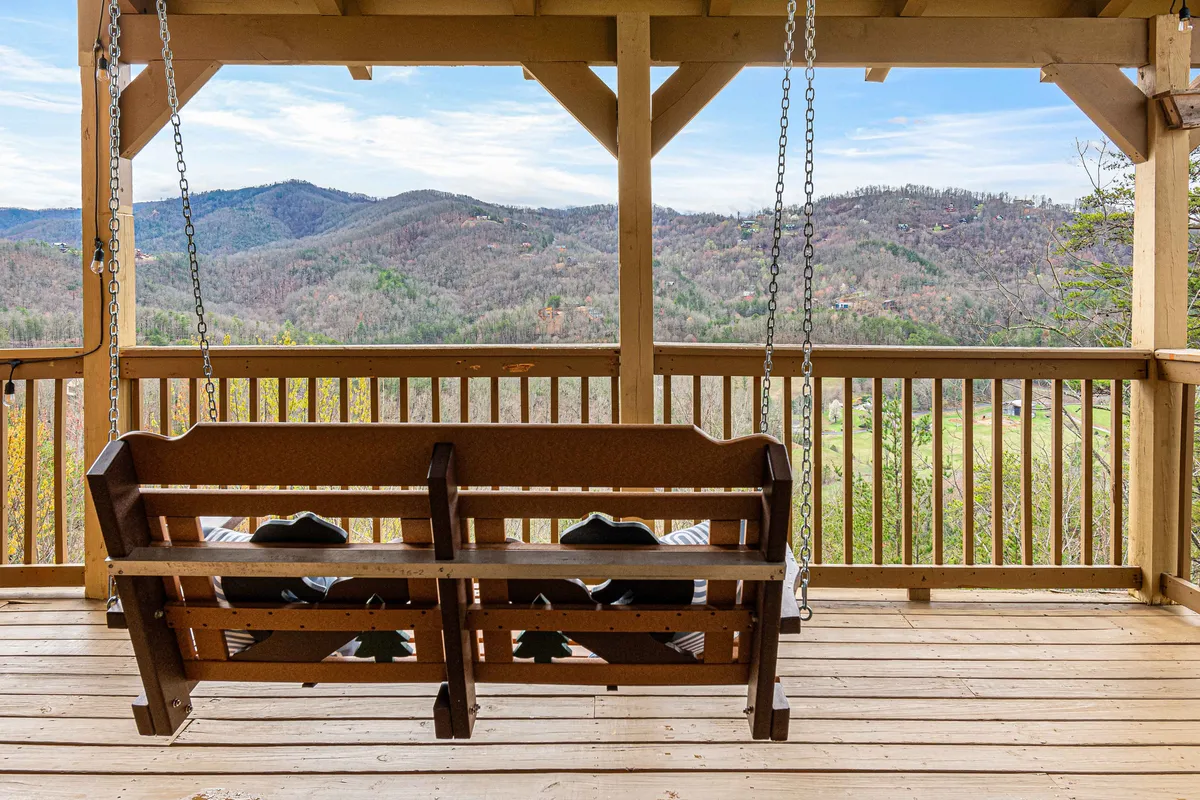 A serene exterior shot featuring a swinging bench on a wooden deck overlooking a sweeping mountain view. The setting is ideal for moments of quiet relaxation, reflection, or informal group chats, with the natural landscape fostering a sense of escape and inspiration.