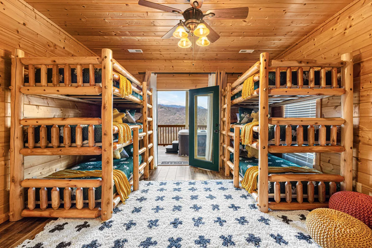 A friendly, communal bunk room with stacked bunk beds, a decorative rug, and an open door leading to an outdoor area. The atmosphere is playful yet relaxing, inviting groups or families to share the space comfortably.