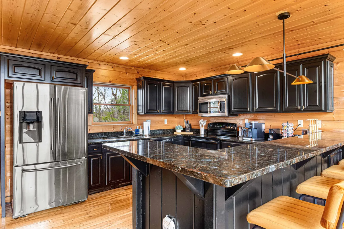 A welcoming kitchen scene featuring granite countertops, sleek black cabinetry, and modern stainless steel appliances. Bar stools line the breakfast bar, inviting guests to gather and converse. The space is well-lit and feels both spacious and cozy, perfectly suited for family cooking, snacking, and socializing.