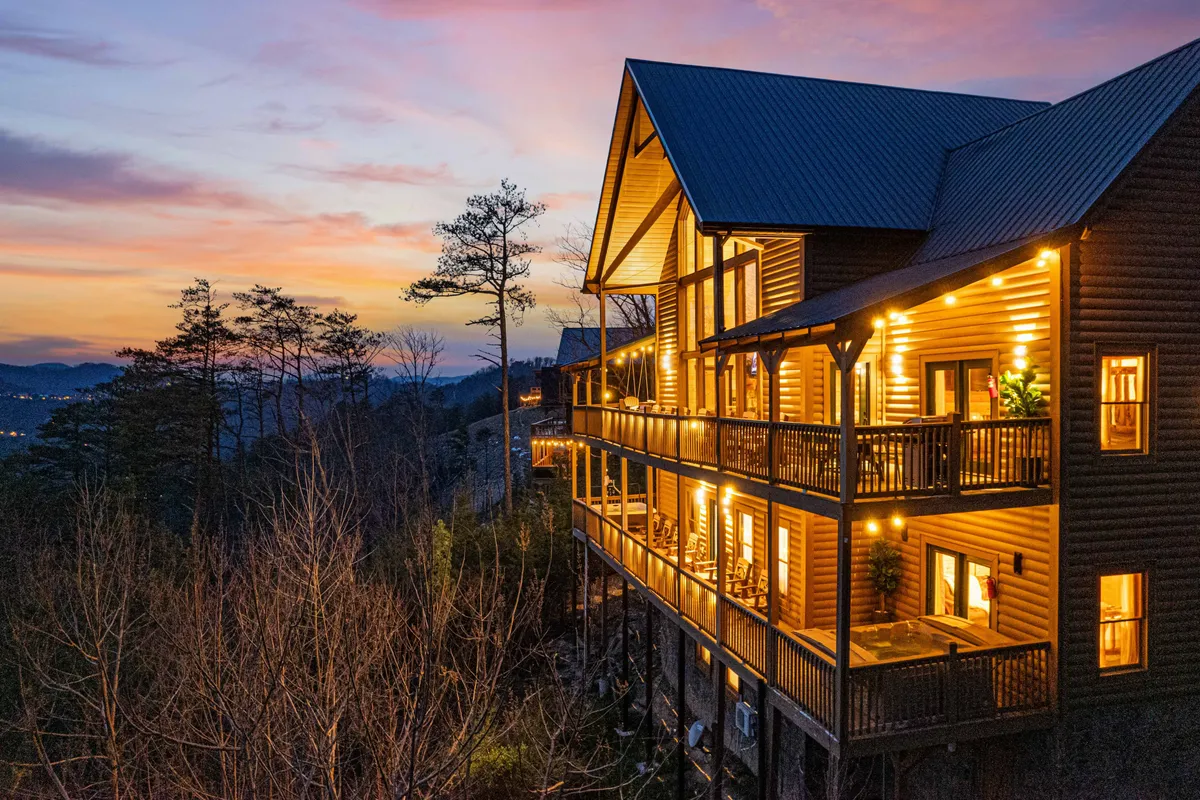 This image features the cabin's wooden facade with inviting balconies illuminated by warm lights against a stunning sunset sky. The scene promises coziness, outdoor gathering spots, and a welcoming ambiance for guests returning after exploring the Smokies.