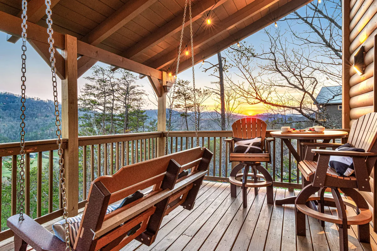 An inviting exterior space with a swing bench and high-top table positioned to face a dramatic sunset over the mountains. The arrangement suggests a venue for outdoor dining, casual meetups, or group discussions, emphasizing the social and scenic aspects of the retreat experience.