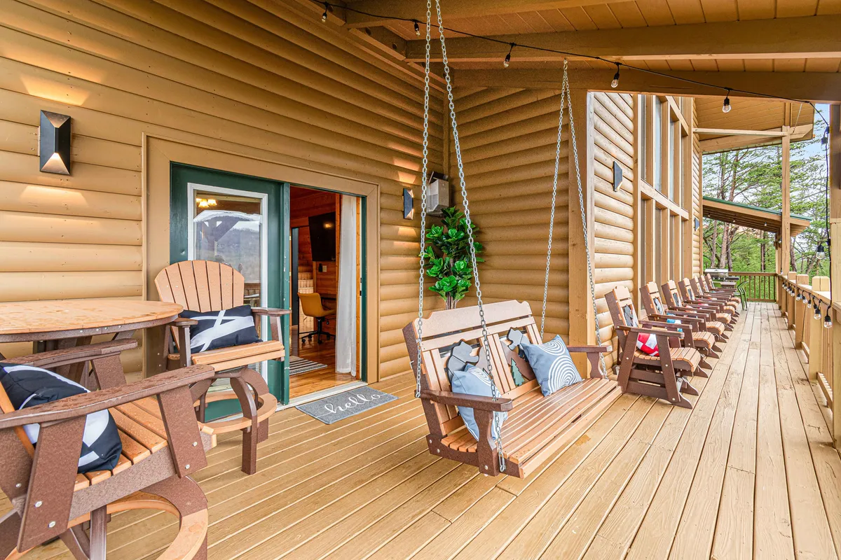 A cozy exterior porch area featuring swing chairs and a dining table, positioned by the entrance door and surrounded by lush greenery. The setting exudes comfort and an inviting atmosphere, with space for relaxing or chatting while appreciating the views and fresh mountain air.