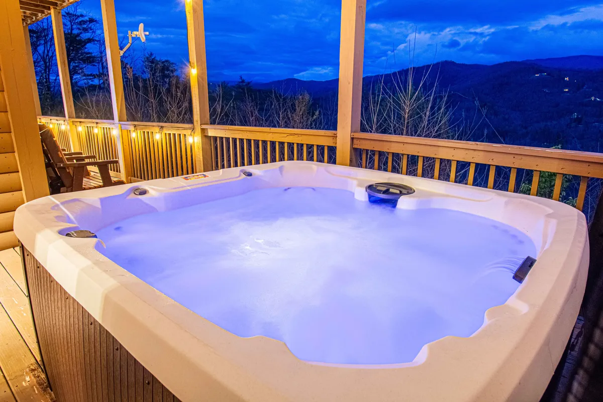 A serene mountain deck with a large hot tub overlooking rolling hills and an expansive sky. The scene features friends or family relaxing together, enjoying both the view and the soothing waters, possibly as the sun sets.